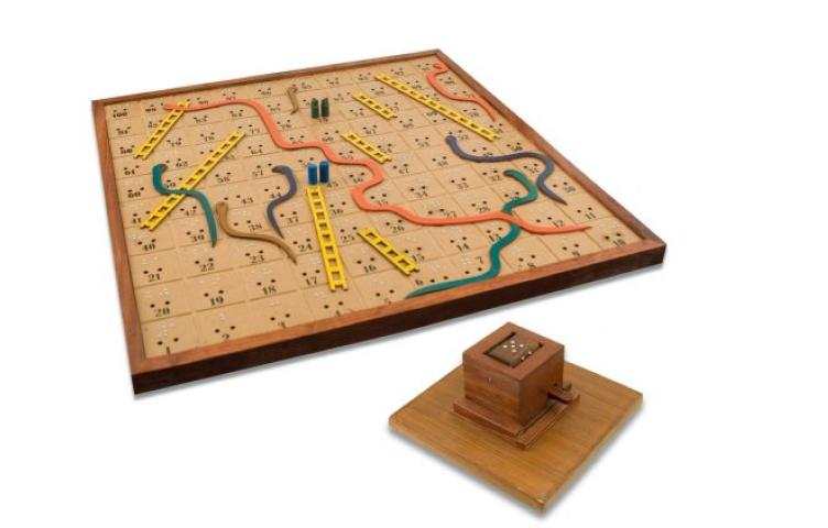 A wooden snakes and ladders board with braille markings and a tactile dice roller.